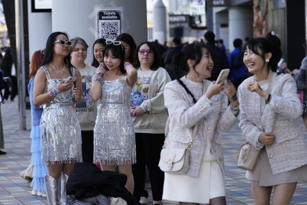 People wait in line near a poster to have their photo taken with others, right, in front of a selfie before Taylor Swift's concert at the Tokyo Dome in Tokyo, Saturday, Feb. 10, 2024. (AP Photo /Hiro Komae)